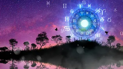 Blauer Horoskopkreis umgeben von einer Galaxie und Bäumen - Foto: Peach_iStock/iStock