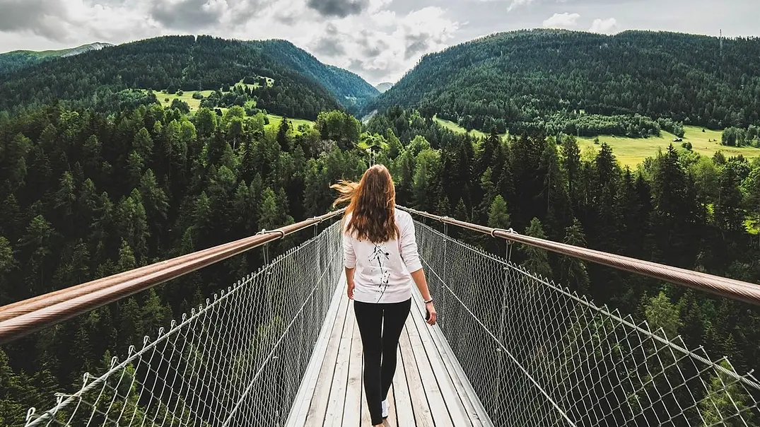 Frau läuft über Brücke mit Blick auf Bäume und Berge - Foto: Jana Vorackova/iStock Frau läuft über Brücke mit Blick auf Bäume und Berge - Foto: Jana Vorackova/iStock