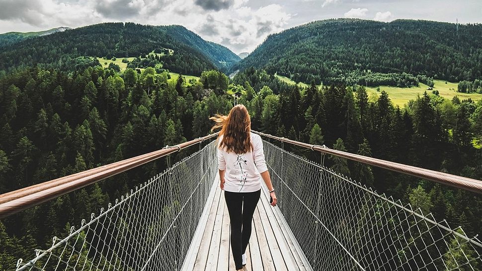 Frau läuft über Brücke mit Blick auf Bäume und Berge - Foto: Jana Vorackova/iStock