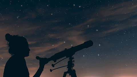 Silhouette einer Frau mit einem Teleskop vor Sternenhimmel - Foto: Allexxandar/iStock