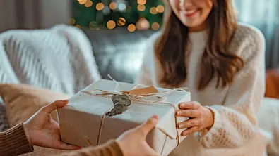Frau in einem hellen Pullover bekommt ein Geschenk überreicht - Foto: iStock/oatawa