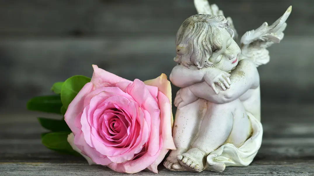 Kleine Engelstatue neben einer pinken Rose - Foto: izzzy71 / AdobeStock Kleine Engelstatue neben einer pinken Rose - Foto: izzzy71 / AdobeStock