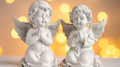 Zwei kleine Engel-Statuen vor einem leuchtenden Hintergrund - Foto: AdobeFirefly (generiert mit KI)