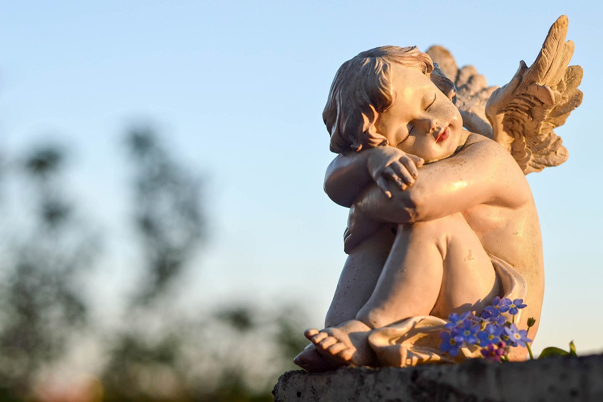 Hockende Engelstatue sitzt mit blauer Blume auf einem Felsvorsprung