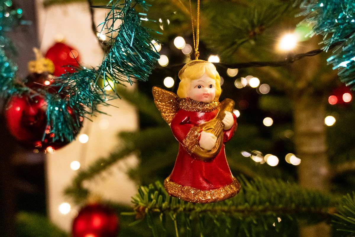 Roter Weihnachtsengel in einem Baum mit Lichtern und anderen Ornamenten im Hintergrund