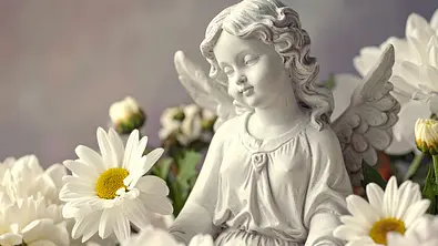 kleine Engelstatue umgeben von Blumen - Foto: AdobeFirefly (generiert mit KI)