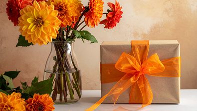 Geburtstagsgeschenk neben einem Strauß mit orangenen Blumen - Foto: AdobeFirefly (generiert mit KI)