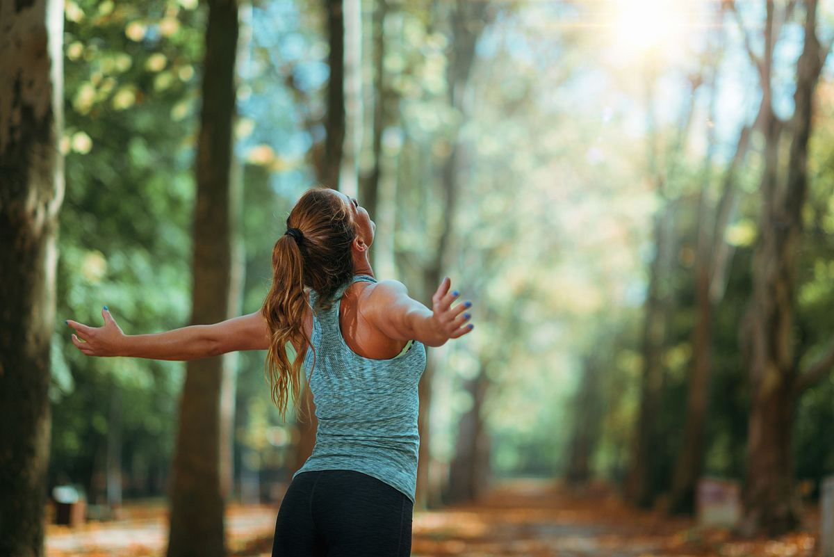 Frau steht im Wald und breitet die Arme aus