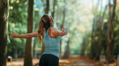 Frau steht im Wald und breitet die Arme aus - Foto: Microgen / AdobeStock