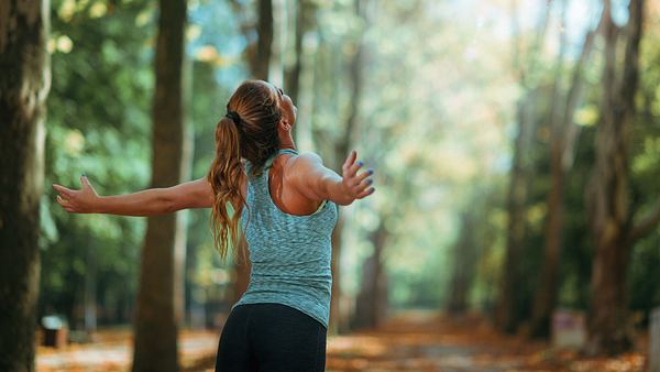 Frau steht im Wald und breitet die Arme aus - Foto: Microgen / AdobeStock