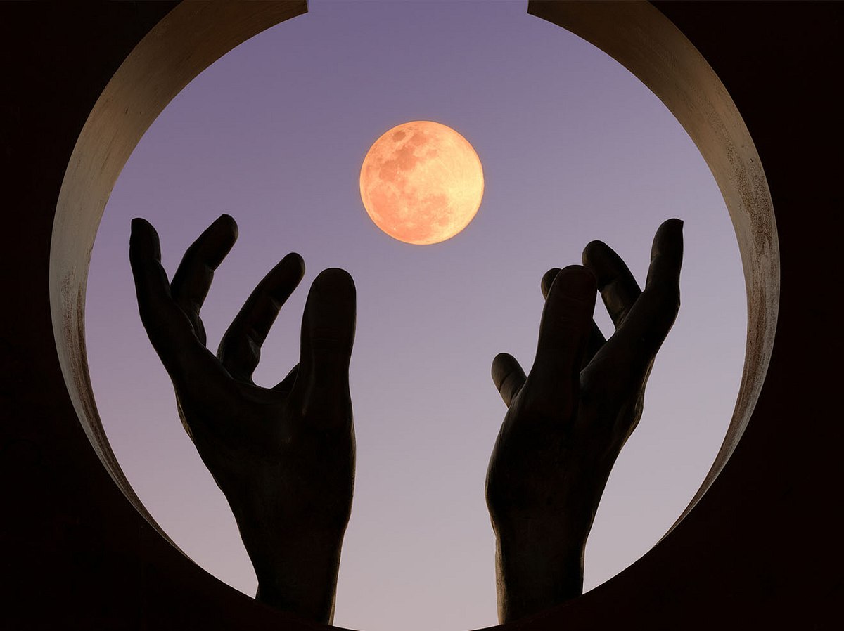 Hände greifen in einem runden Fenster nach dem Vollmond