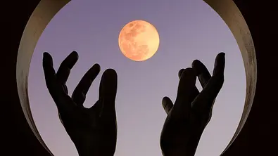 Hände greifen in einem runden Fenster nach dem Vollmond - Foto: Francisco Jose Garrido Angulo / iStock