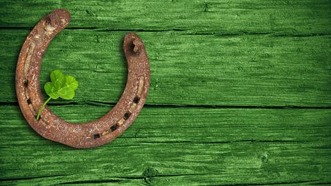 Hufeisen und Glücksklee vor einem grünen Holz-Hintergrund - Foto: Marina Lohrbach / AdobeStock