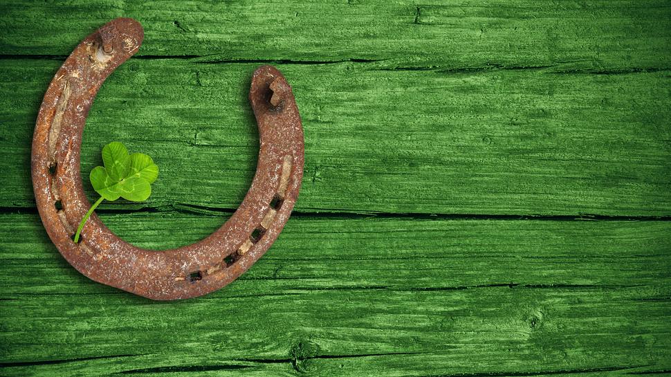 Hufeisen und Glücksklee vor einem grünen Holz-Hintergrund - Foto: Marina Lohrbach / AdobeStock