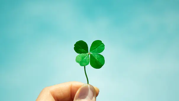  Zwischen zwei Fingern ruht ein Kleeblatt, der blaue Hintergrund lässt das zarte Grün besonders leuchten. - Foto: loveallyson/iStock