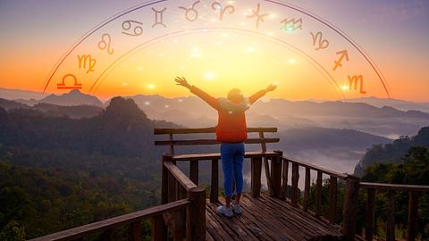 Frau streckt Ihre Arme in den Himmel. Im Hintergrund ist eine Berglandschaft über der ein Sternzeichen-Kreis im Sonnenuntergang erstrahlt. - Foto: sarayut_sy / AdobeStock