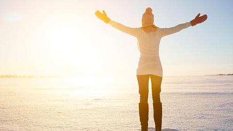 Frau steht mit geöffneten Armen im Schnee und begrüßt die Sonne - Foto: AlekZotoff / iStock