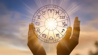 Zwei Händen strecken sich in Richtung Himmel und umrahmen eine Grafik des astrologischen Tierkreises, durch die die Sonne leuchtet. - Foto: sarayut/iStock