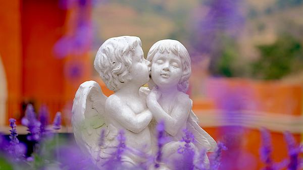 Zwei Engelfiguren küssen sich in einem Blumengarten - Foto: Thakkura Podjanapon / iStock