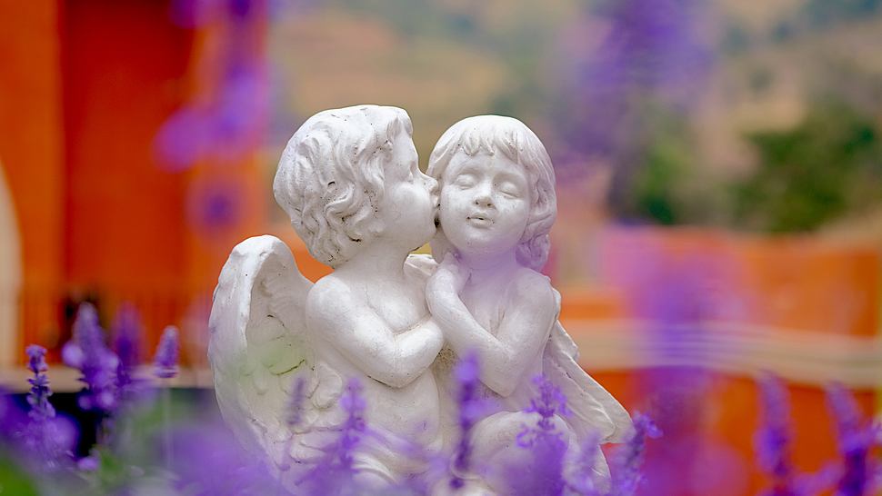 Zwei Engelfiguren küssen sich in einem Blumengarten - Foto: Thakkura Podjanapon / iStock