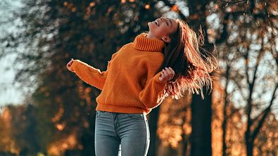 Frau in einem orangenen Rollkragen Pullover steht glücklich in einem herbstlichen Park - Foto: Vasyl / AdobeStock