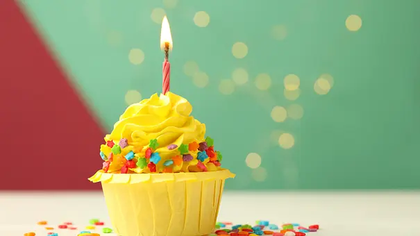 Cupcake mit gelber Creme, bunten Streuseln und einer Kerze - Foto: iStock/Olga Yastremska