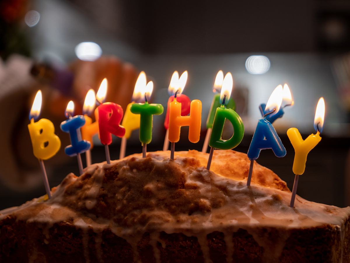 Bunte Kerzen in Buchstabenform, die Happy Birthday schreiben, brennen auf einem Kuchen.