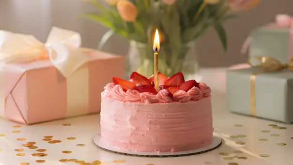 Eine rosa Torte mit Erdbeeren und einer brennenden Kerze steht auf einem festlich dekorierten Tisch neben Geschenken und einem Tulpenstrauß. - Foto: AdobeFirefly (generiert mit KI) Eine rosa Torte mit Erdbeeren und einer brennenden Kerze steht auf einem festlich dekorierten Tisch neben Geschenken und einem Tulpenstrauß. - Foto: AdobeFirefly (generiert mit KI)