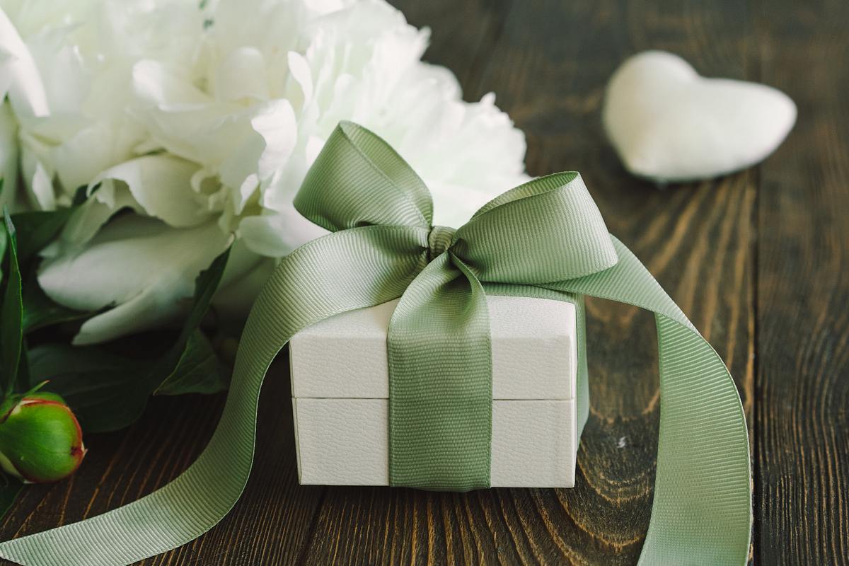 Ein Geschenk mit grüner Schleife und weißen Blumen auf einem Holztisch