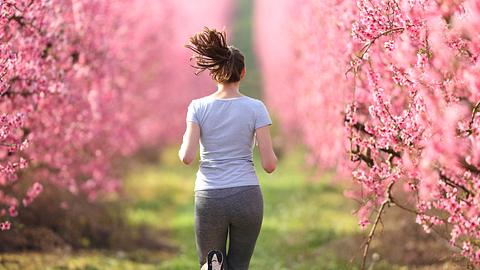 Eine Frau joggt über ein Feld umgeben von Blüten - Foto: Pheelings Media/iStock