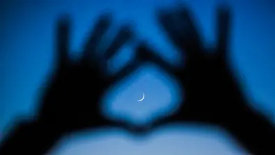 Hände formen einen Kreis um einen Mond am Himmel - Foto: amygdala-imagery / iStock