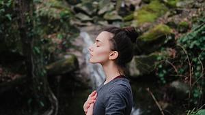 Frau, die mit den Händen auf der Brust in einem Wald durchatmet - Foto: Yolya / iStock