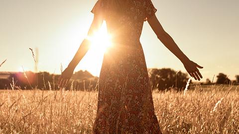 Frau steht auf einer Wiese im Sonnenlicht - Foto: iStock/kieferpix