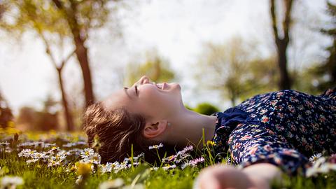 Lächelnde Frau liegt ausgestreckt auf einer Wiese voller Gänseblümchen - Foto: iStock/hobo_018