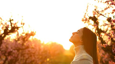 Frau richtet ihr Gesicht dem Himmel entgegen bei Sonnenaufgang - Foto: iStock/Pheelings Media