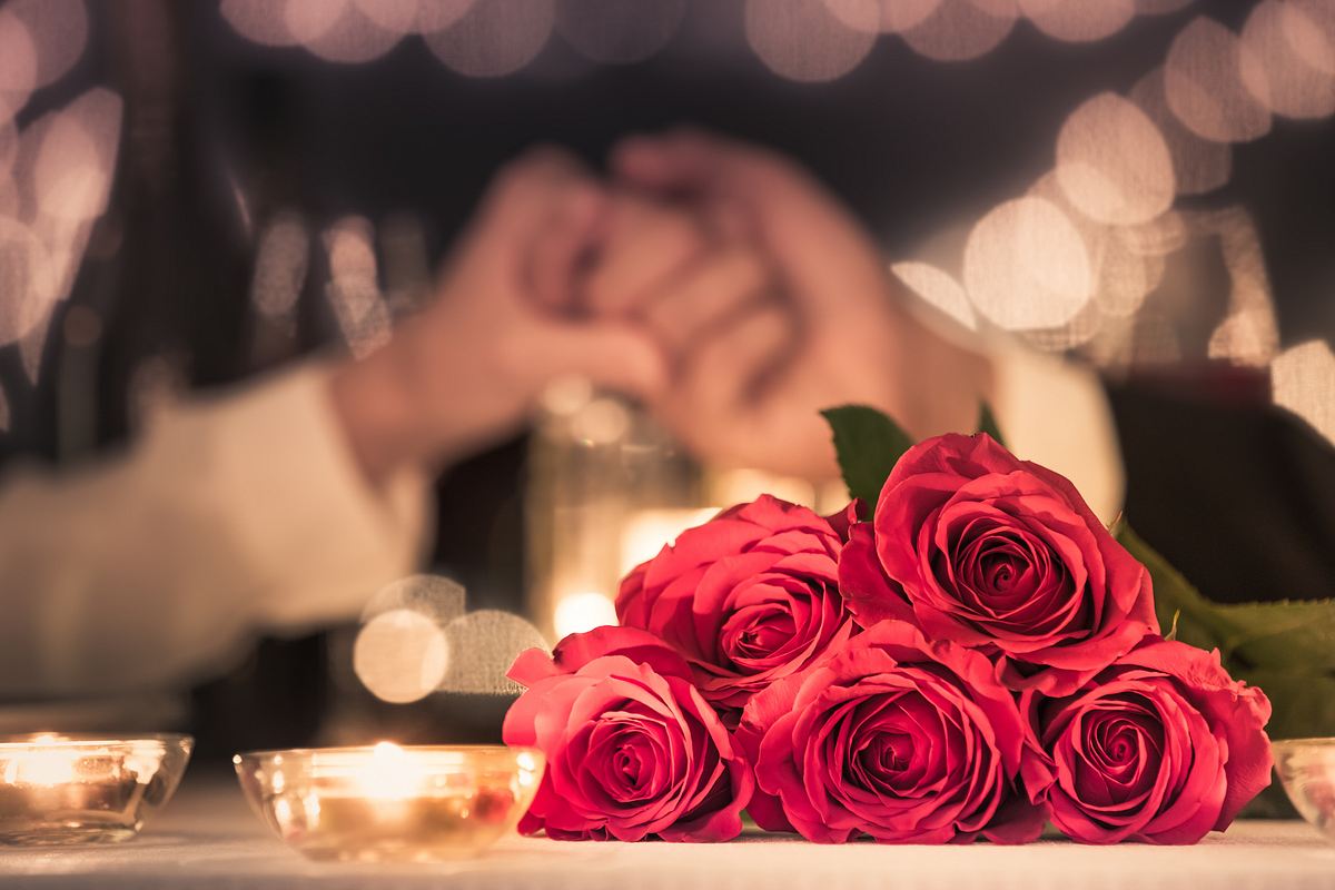 Rote Rosen im Vordergrund, zwei Hände, die sich greifen im Hintergrund