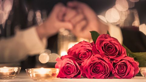 Rote Rosen im Vordergrund, zwei Hände, die sich greifen im Hintergrund - Foto: iStock/kieferpix
