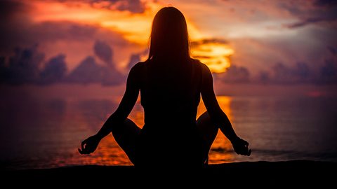 Frau meditiert am Strand im Sonnenuntergang - Foto: guruXOX/ AdobeStock