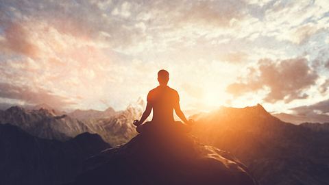 Mann sitzt meditierend in einer Berglandschaft - Foto: Photocreo Bednarek / Adobe Stock