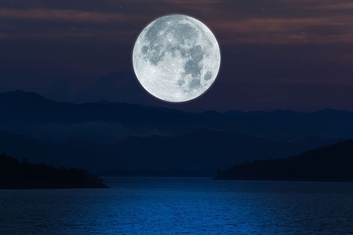 Vollmond steht bei Nacht über einem dunklen See