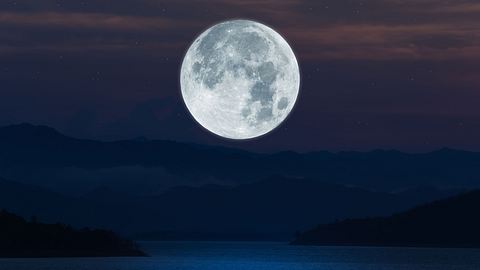 Vollmond steht bei Nacht über einem dunklen See - Foto: Onkamon / AdobeStock
