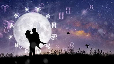 Sternzeichen-Rad vor einem Sternenhimmel am Wasser. Davor die Silhouetten eines glücklichen Paares. er trägt sie auf Händen. - Foto: Peach_iStock/iStock
