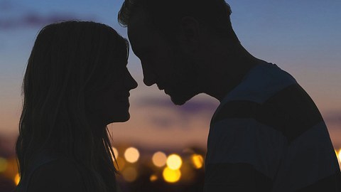 Silhouetten von einem jungen Paar küssen mit Stadtpanorama im Hintergrund - Foto: m-gucci / iStock