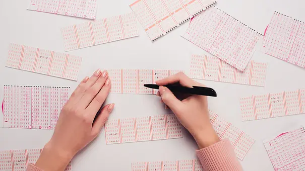 Eine Person füllt mehrere Lottoscheine auf einem Tisch aus und setzt mit einem Stift Kreuzchen auf den Feldern. - Foto: LIGHTFIELD STUDIOS / AdobeStock Eine Person füllt mehrere Lottoscheine auf einem Tisch aus und setzt mit einem Stift Kreuzchen auf den Feldern. - Foto: LIGHTFIELD STUDIOS / AdobeStock