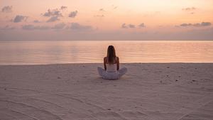 Frau sitzt meditierend am Strand - Foto: iStock/ Mystockimages