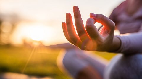 Frau sitzt auf einer grünen Wiese und hält die Hände in Meditationspose - Foto: Isbjorn / iStock