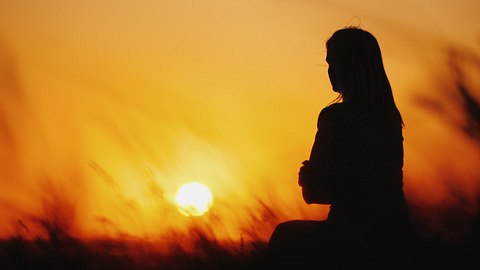 Meditierende Frau vor einem Sonnenuntergang sitzend - Foto: iStock/ StockSeller_ukr