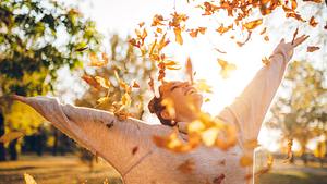 Frau wirft herbstliche Blätter in die Luft - Foto: iStock/urbazon