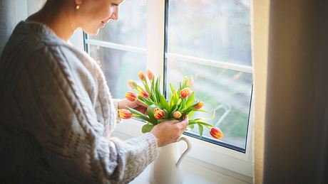 Frau schaut sich Tulpen in einer Vase an - Foto: Rike_/iStock