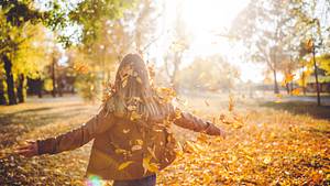 Frau bewegt sich durch in die Luft geworfenes Herbstlaub - Foto: urbazon/iStock